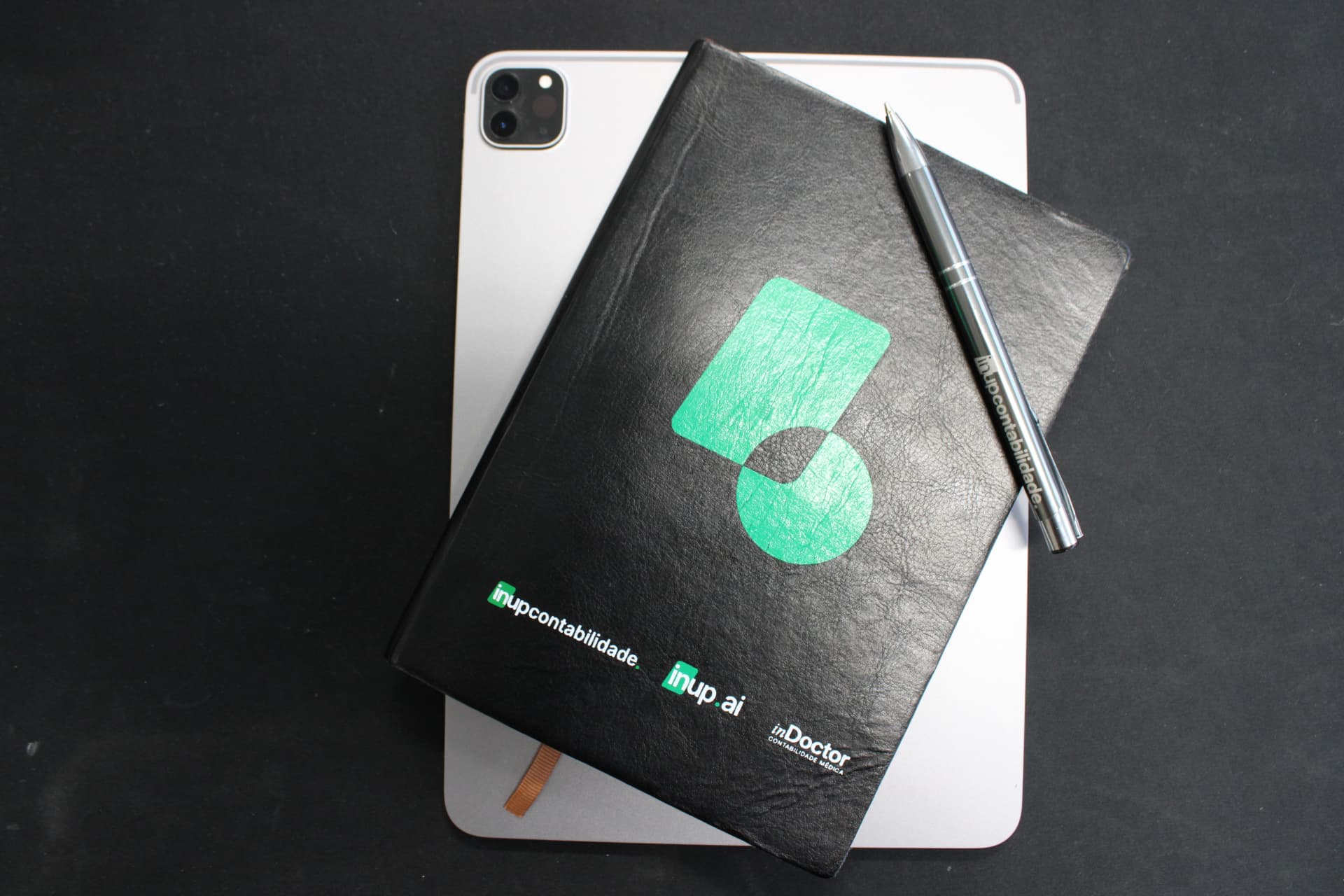 Caderno e tablet da InUP sobre mesa escura